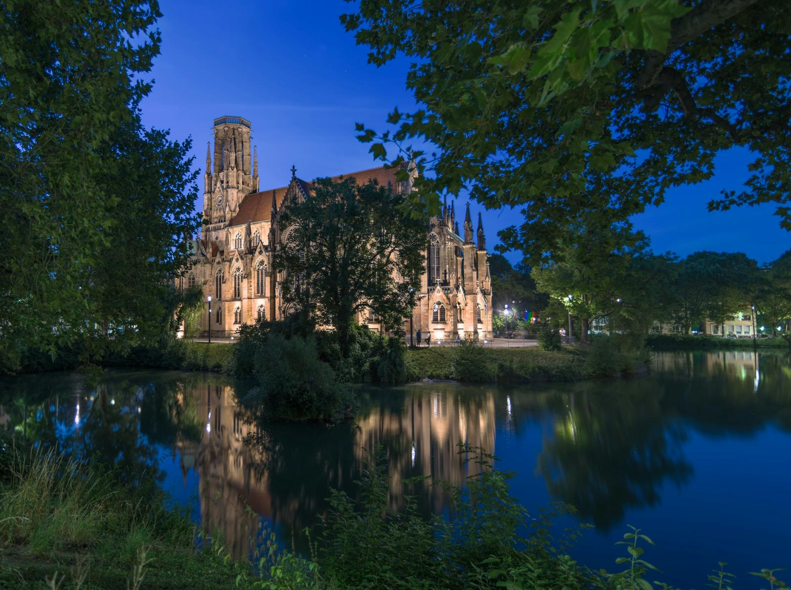 St John's Church illuminated at night, reflecting on a tranquil Stuttgart lake.