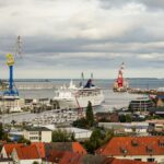 Aerial view of a bustling harbor with ferries and vibrant red-tiled rooftops under a cloudy sky.